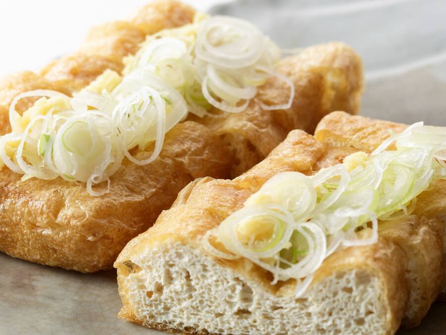 En närbild på en maträtt, troligen en panerad och friterad rätt, garnerad med skivad lök.