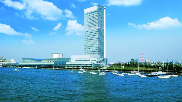 A modern building with a glass facade, situated by a body of water with several boats docked nearby. - Hotel Nikko Niigata (Niigata)