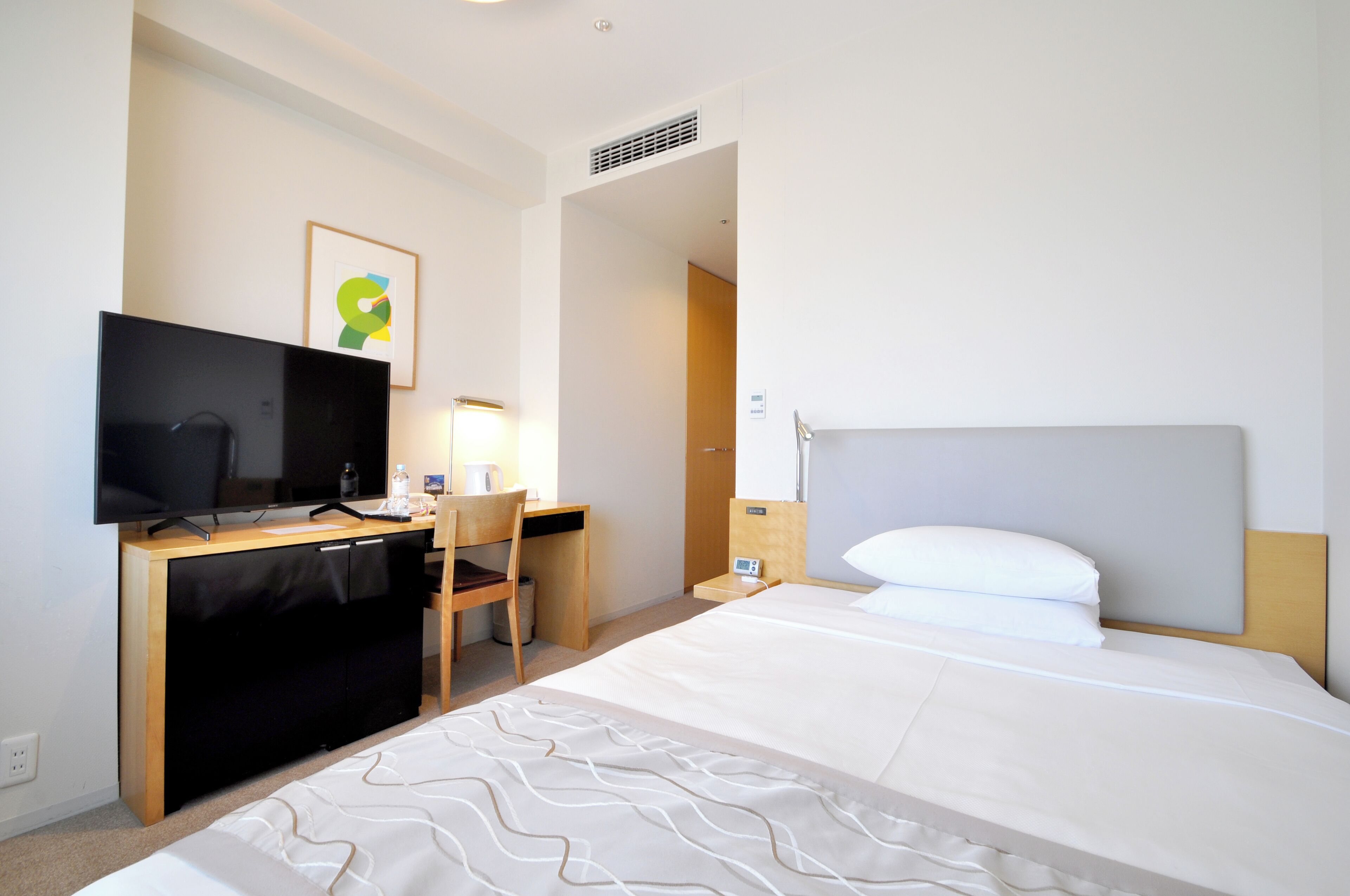 Ein Hotelzimmer mit einem Bett, einem Schreibtisch mit Fernseher, einem Sessel und einem Nachttisch mit Lampe.