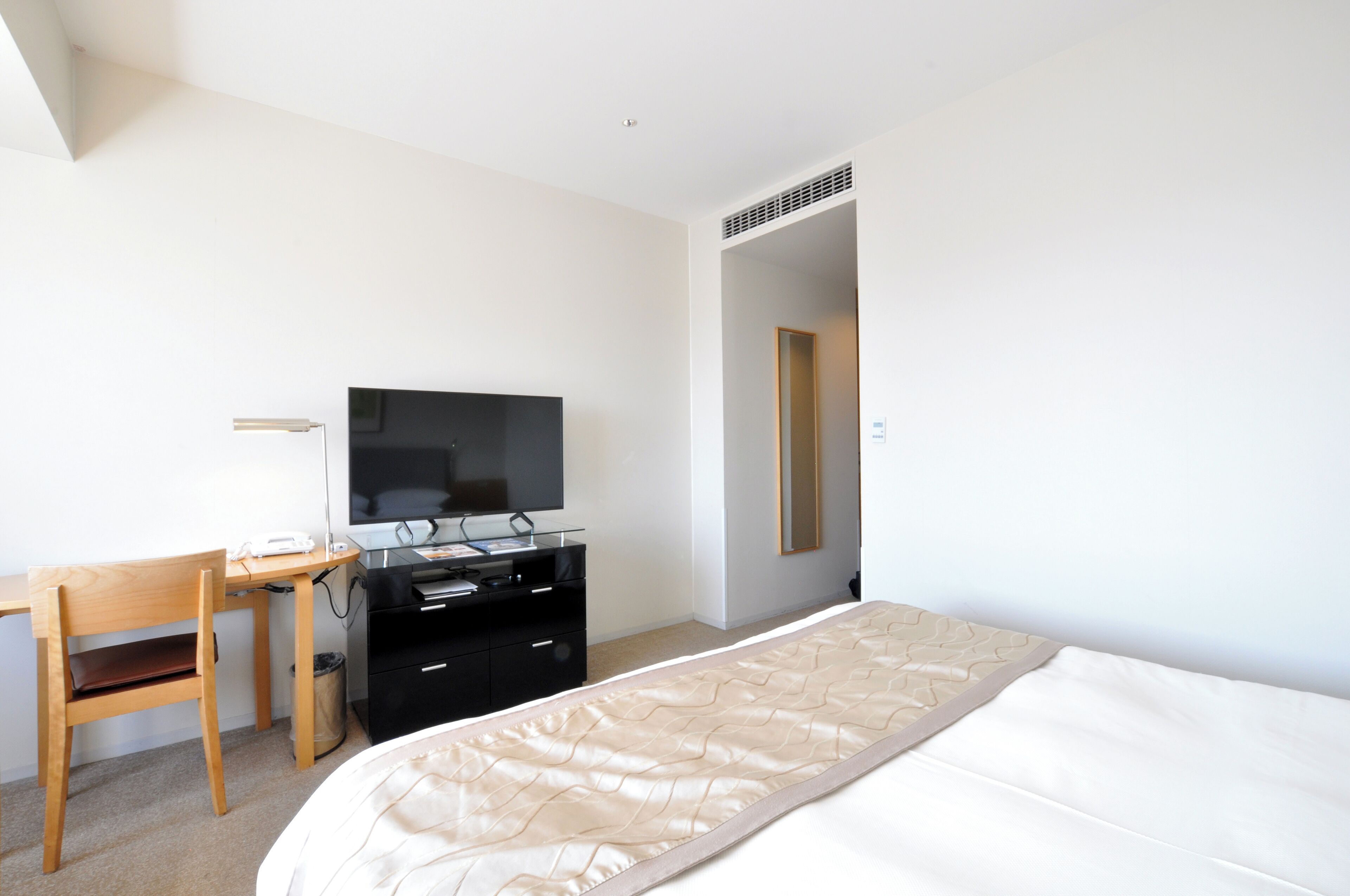 A bedroom with a bed, a desk with a computer, a TV, and a mirror.