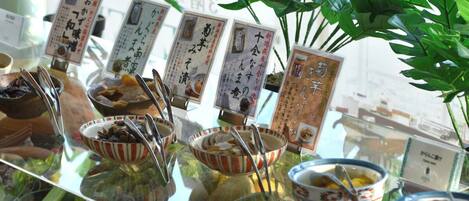 A display of traditional Japanese sweets and desserts with accompanying labels, set against a backdrop of lush green plants.