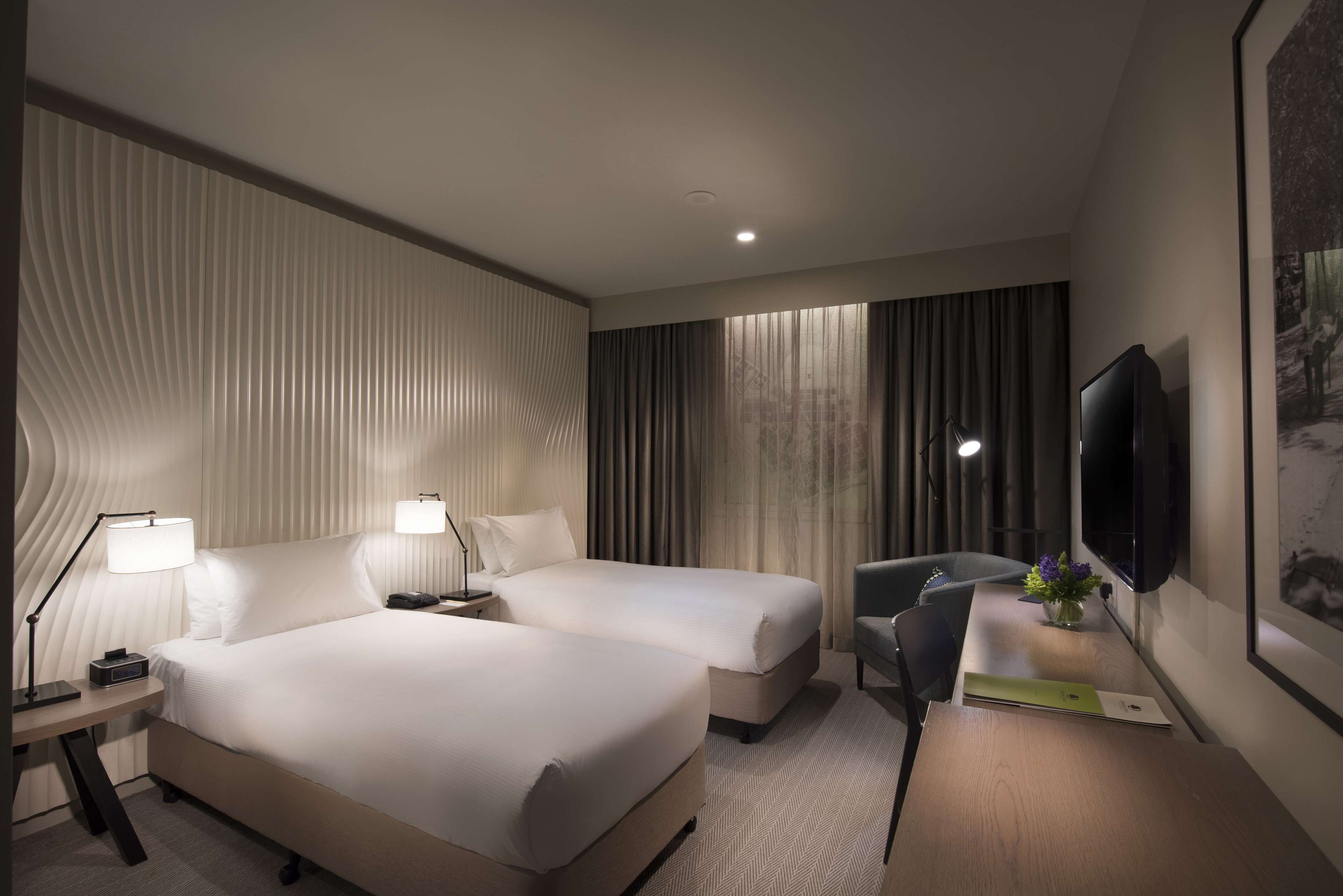A hotel room with two beds, a desk, a chair, a TV, and a window with curtains.