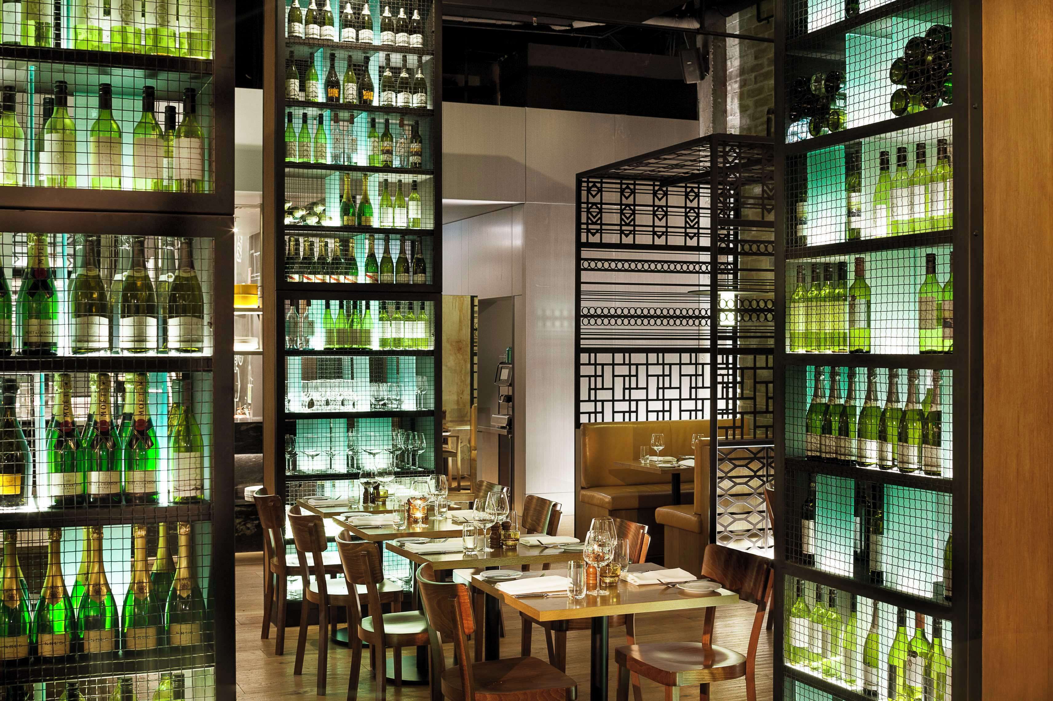 A restaurant interior with multiple dining tables, chairs, and shelves of wine bottles.