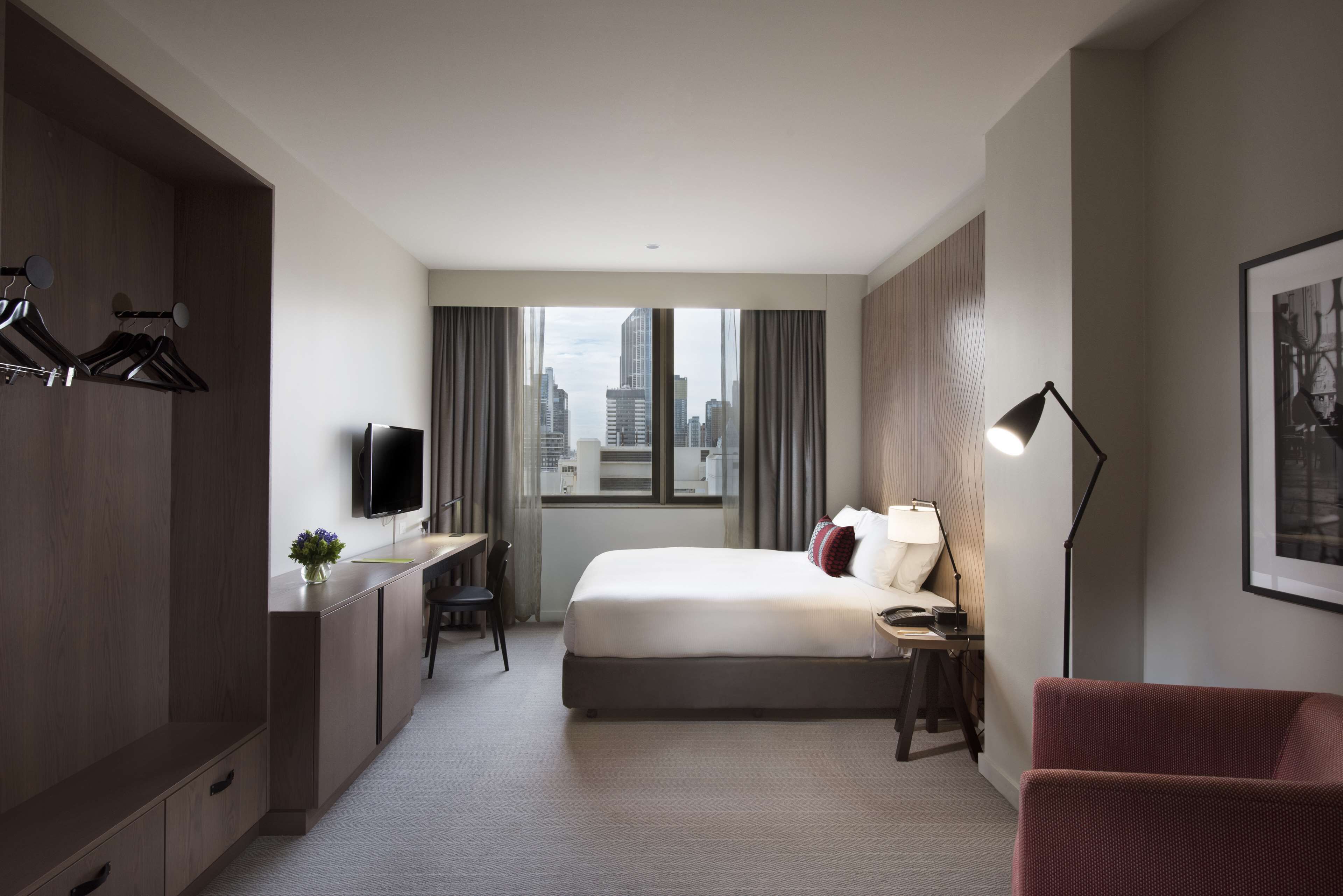 A modern hotel room with a bed, desk, chair, and a city view.