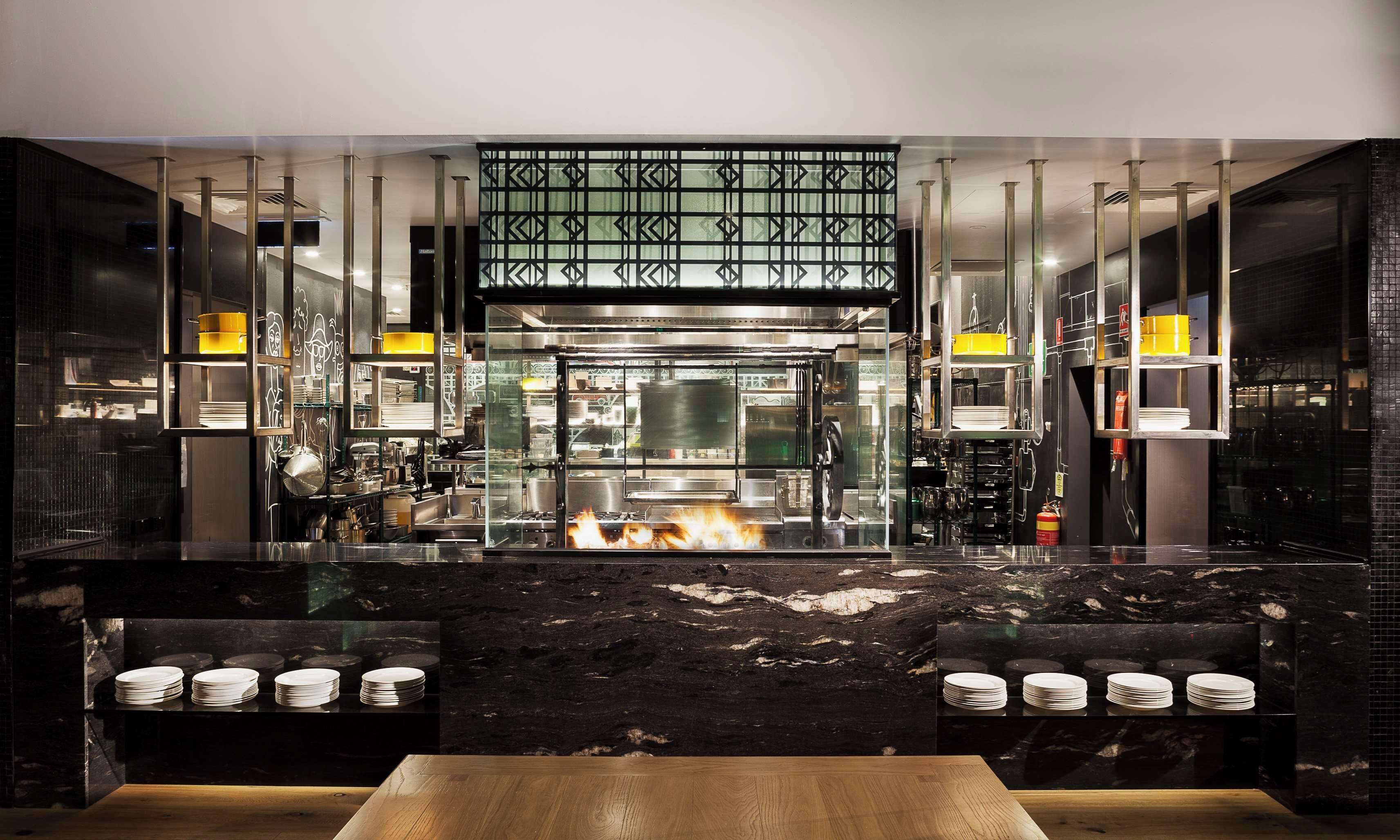 A modern kitchen with a central island, stainless steel appliances, and a visible fire.