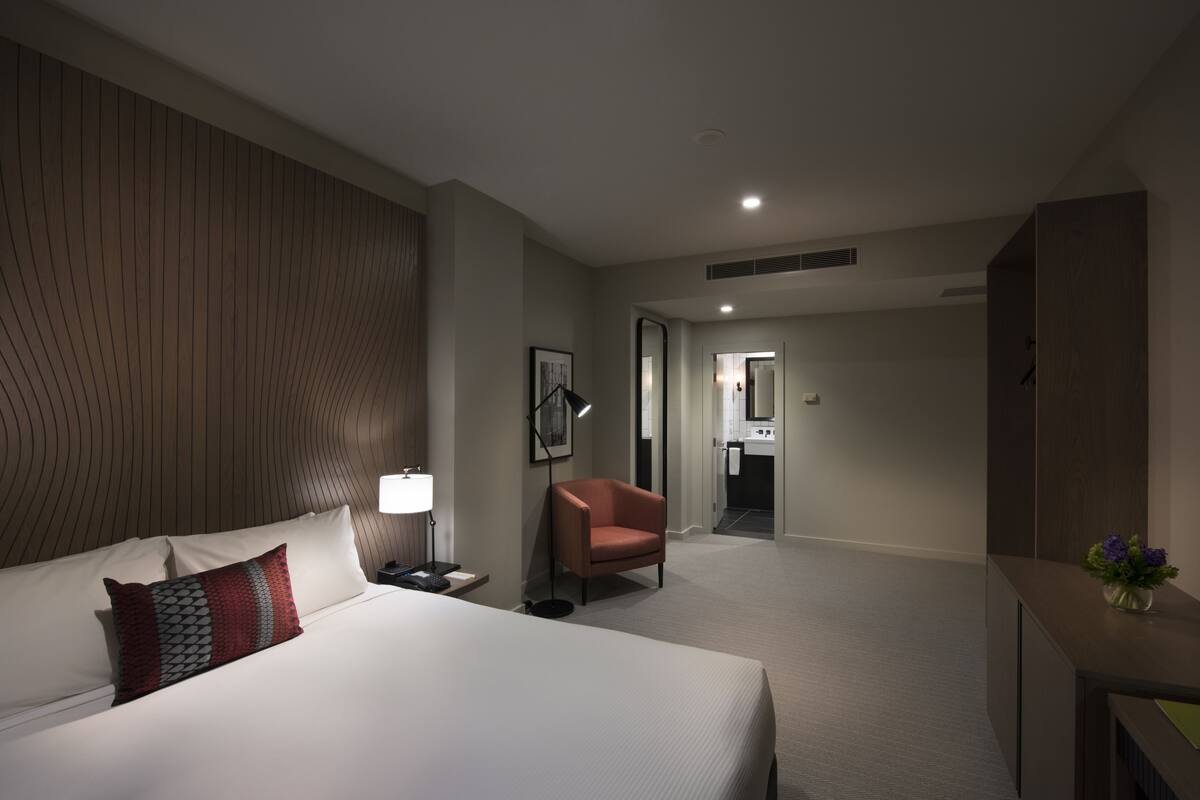 A hotel room with a large bed, a chair, a desk, and a bathroom visible through an open door.