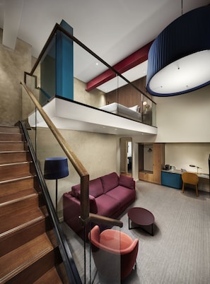 A modern interior with a wooden staircase, a red sofa, a small round table, and a desk with a chair.