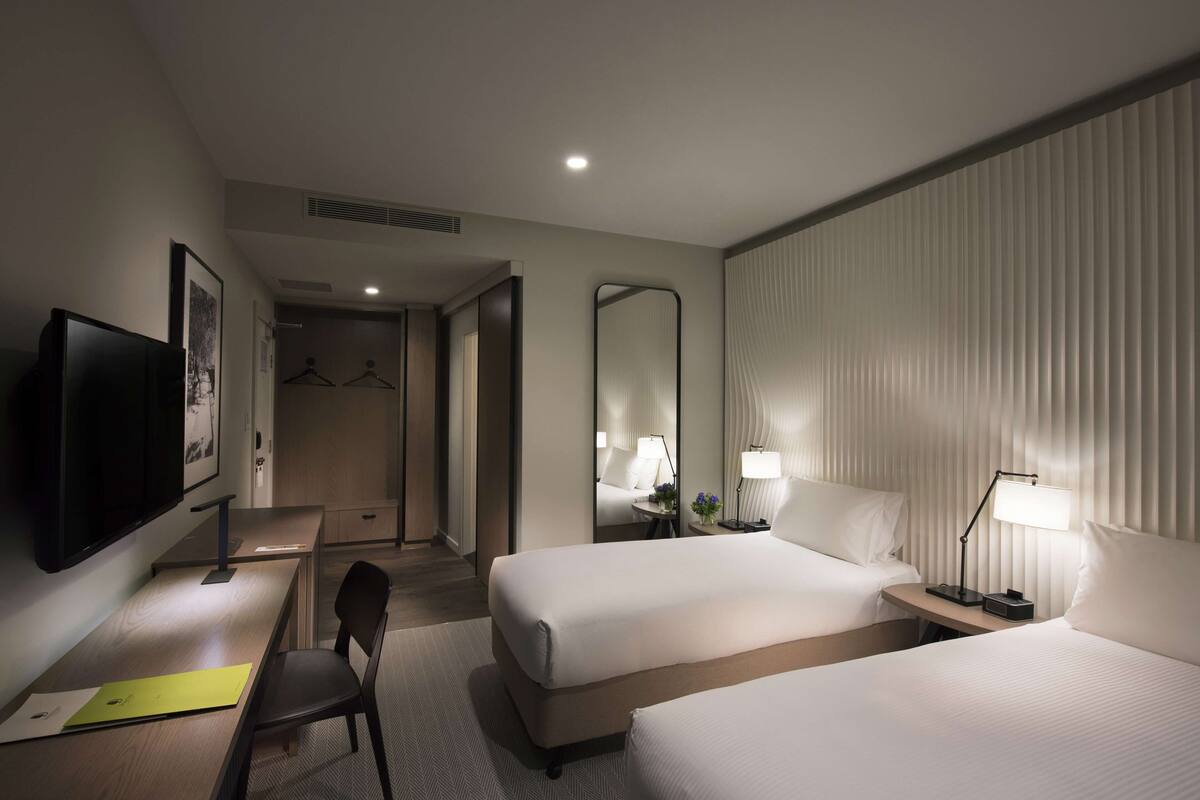 A hotel room with two beds, a desk, a chair, a television, and a mirror.