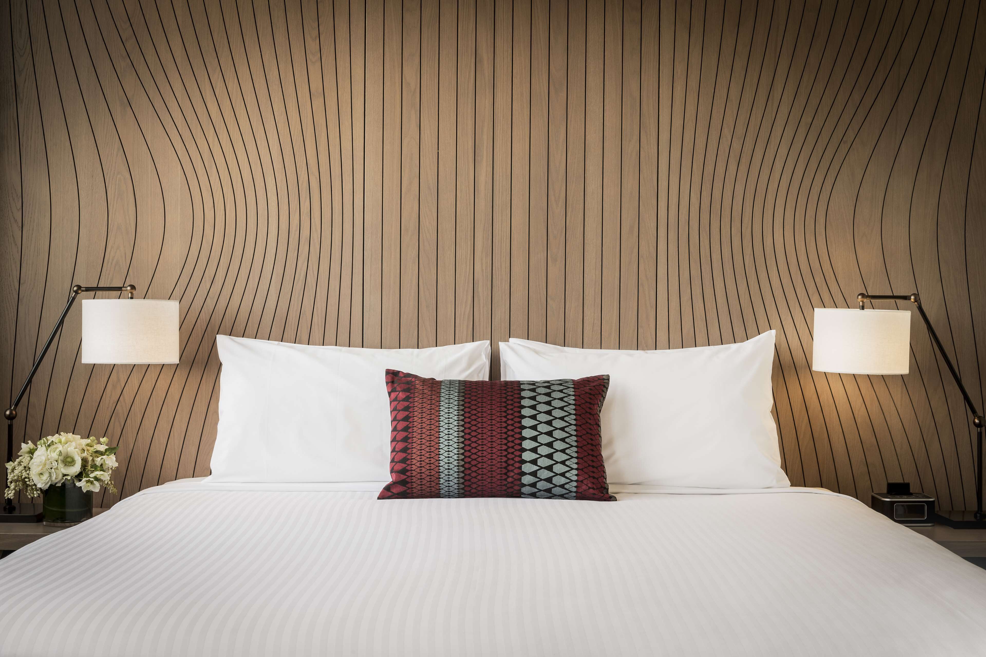 Cama bem arrumada com lençóis brancos, almofada estampada e duas luminárias de cabeceira.