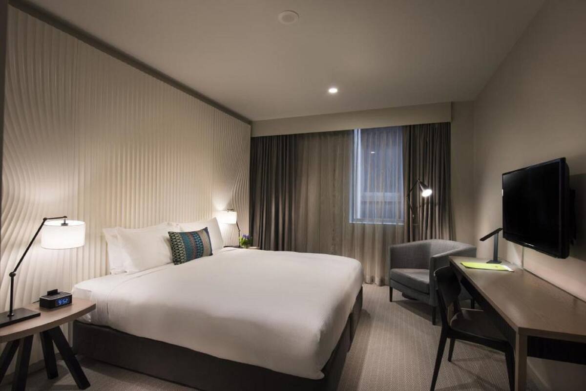 A hotel room with a large bed, a desk, a chair, a TV, and a window with curtains.