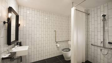 Un baño moderno con pared de azulejos blancos, piso negro, lavamanos blanco con espejo, inodoro y zona de ducha.