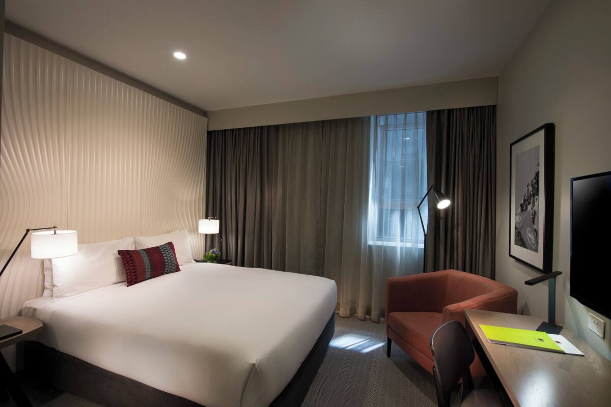 A hotel room with a large bed, a desk, a chair, a TV, and a window with curtains.