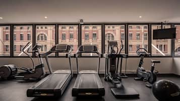 A gym with treadmills, elliptical machines, and a stationary bike, with a cityscape view through large windows.