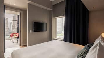 Un cuarto de hotel con una cama grande, un televisor de pantalla plana montado en la pared, una silla roja y vista a la ciudad por una ventana.