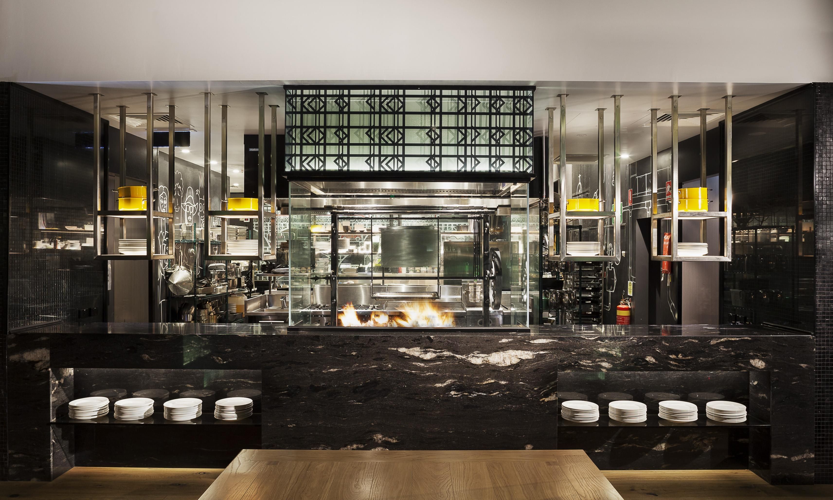 Cocina moderna con una isla central, electrodomésticos de acero inoxidable y una chimenea visible debajo de la encimera.