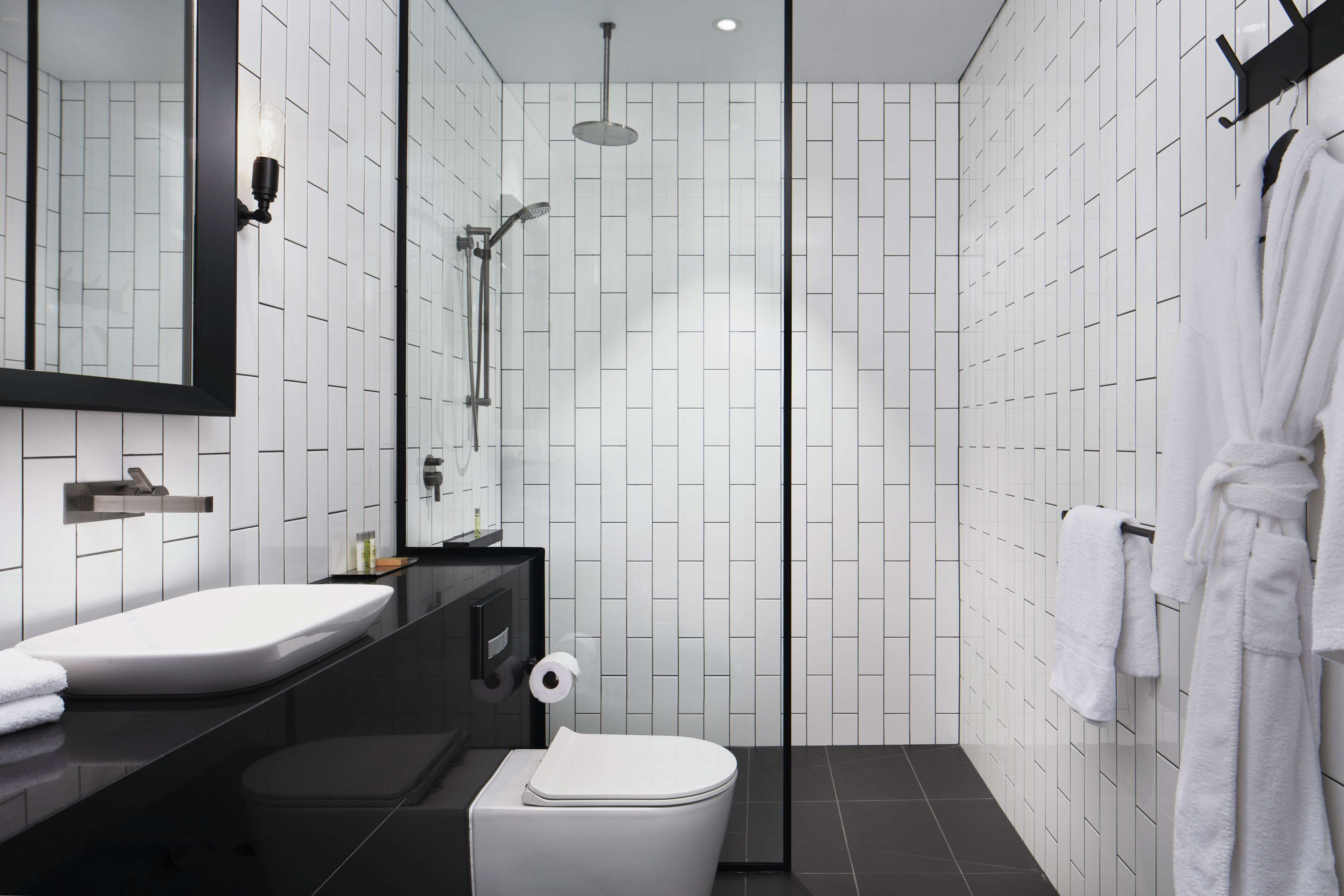 A modern bathroom with a white sink, mirror, and toilet, a shower area, and a towel rack with a robe.