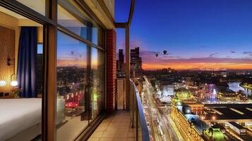 Un balcón con vista a la ciudad al anochecer, mostrando un río, edificios y globos aerostáticos.