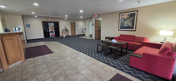 A hotel lobby with a reception desk, a red sofa, a coffee table, and a painting on the wall. - Quality Inn & Suites Eldridge Davenport North (Eldridge)