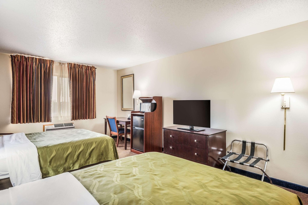 Une chambre d’hôtel avec deux lits, un bureau, une télévision, une commode et une chaise.