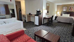A hotel room with a large bed, a separate desk with a chair, a small kitchenette, a bathroom with a bathtub, and a red sofa. - Quality Inn & Suites Eldridge Davenport North (Eldridge)