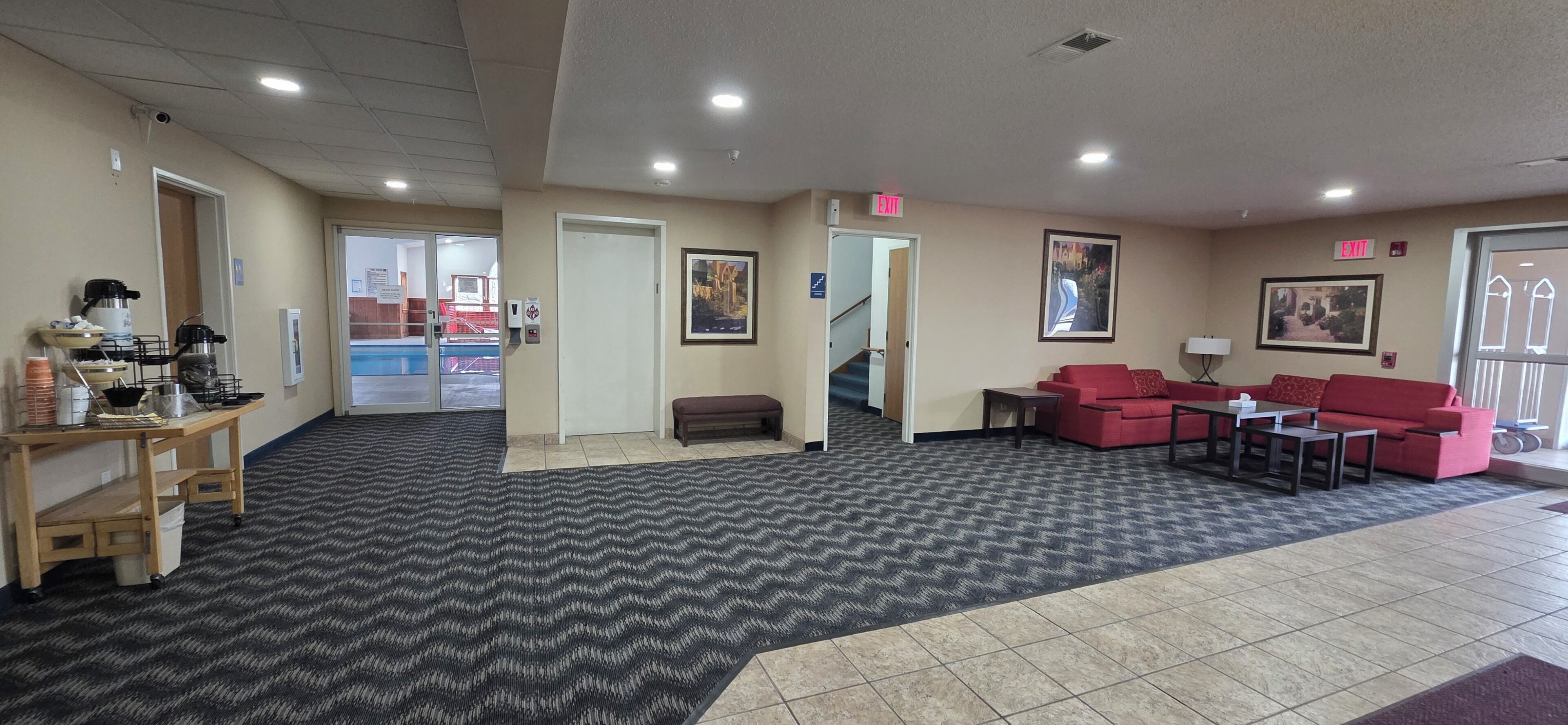 A hotel lobby with a reception desk, a red sofa set, a bench, and a staircase leading to another area.