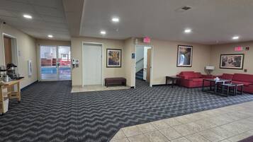 A hotel lobby with a reception desk, a red sofa set, a bench, and a staircase leading to another area.