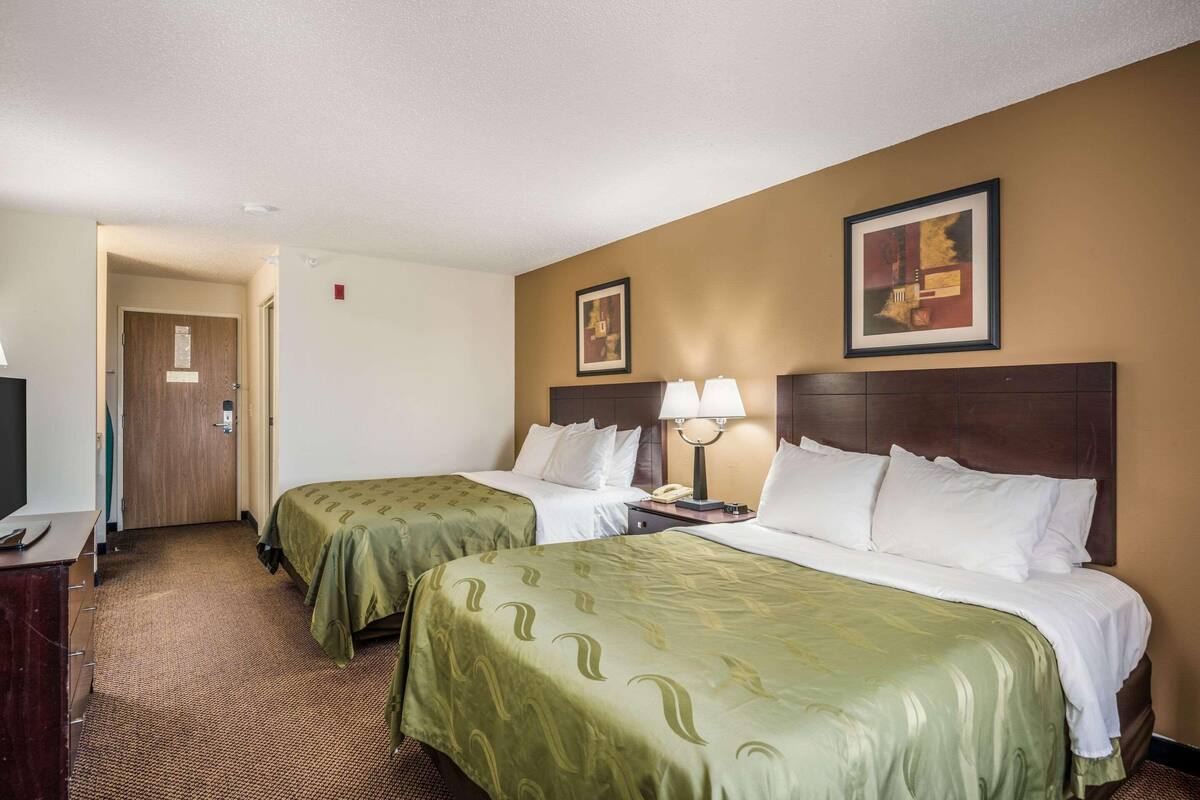 A hotel room with two beds, a desk, a lamp, and a painting on the wall.