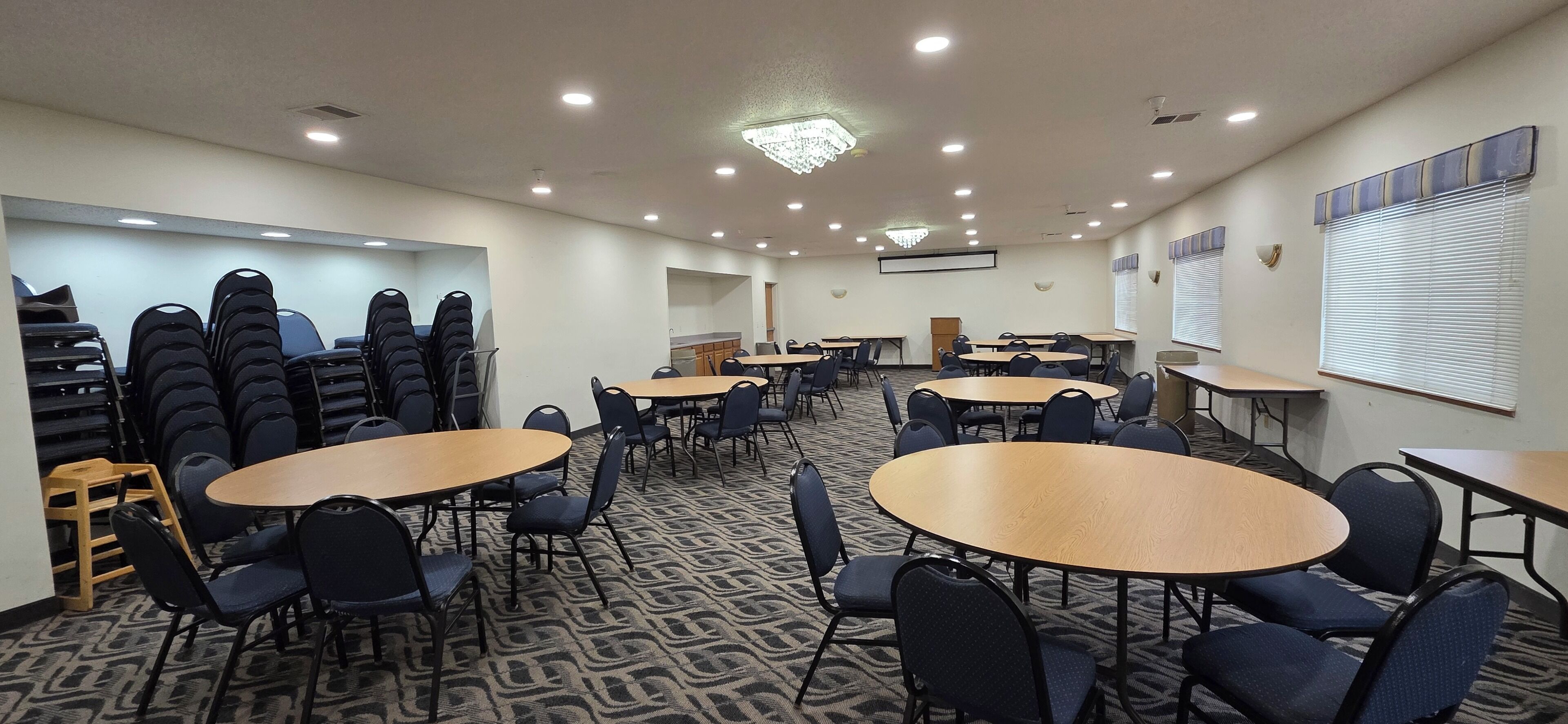 A conference room with multiple tables and chairs, a carpeted floor, and ceiling lights.