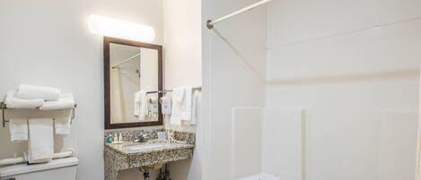 A bathroom with a toilet, sink, mirror, and shower.