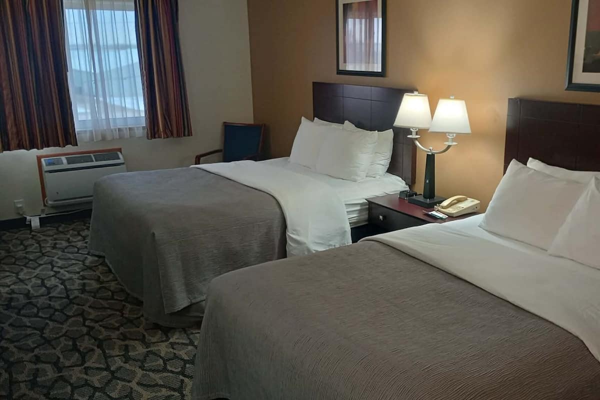 A hotel room with two beds, a nightstand with lamps, a telephone, and a window with curtains.