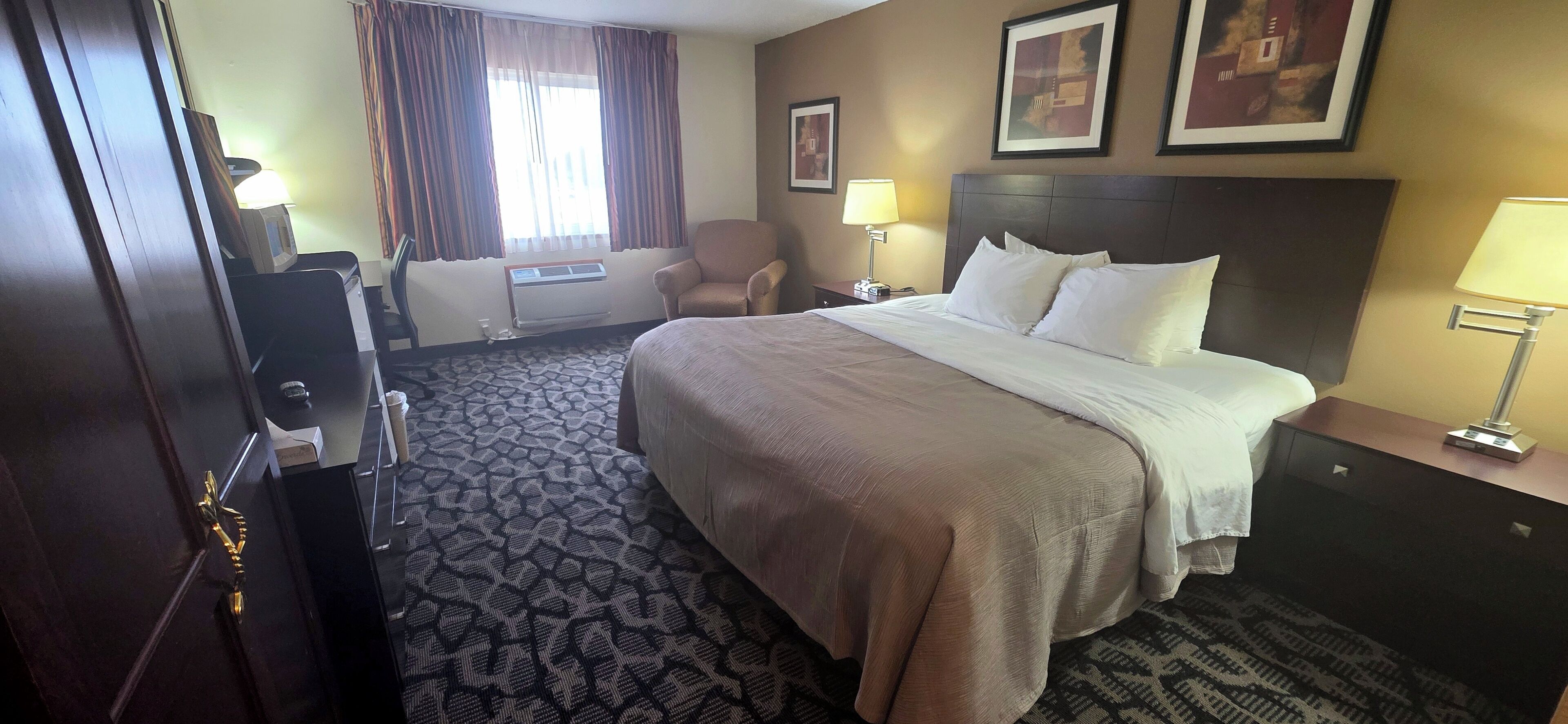 Habitación de hotel con una cama grande, una silla, un escritorio, una lámpara y una ventana con cortinas.