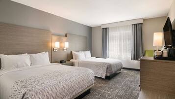 A hotel room with two beds, a desk, a chair, a TV, and a window with curtains.