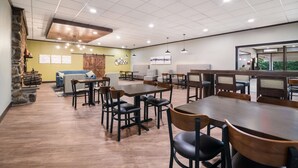 Un vaste espace intérieur doté de nombreuses tables et chaises, d’un mur en pierre sur le côté gauche et d’un plafond en bois.