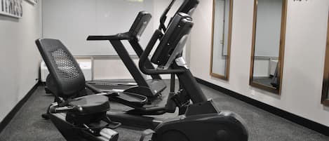 A gym with exercise equipment, a clock, and a mirror on the wall.