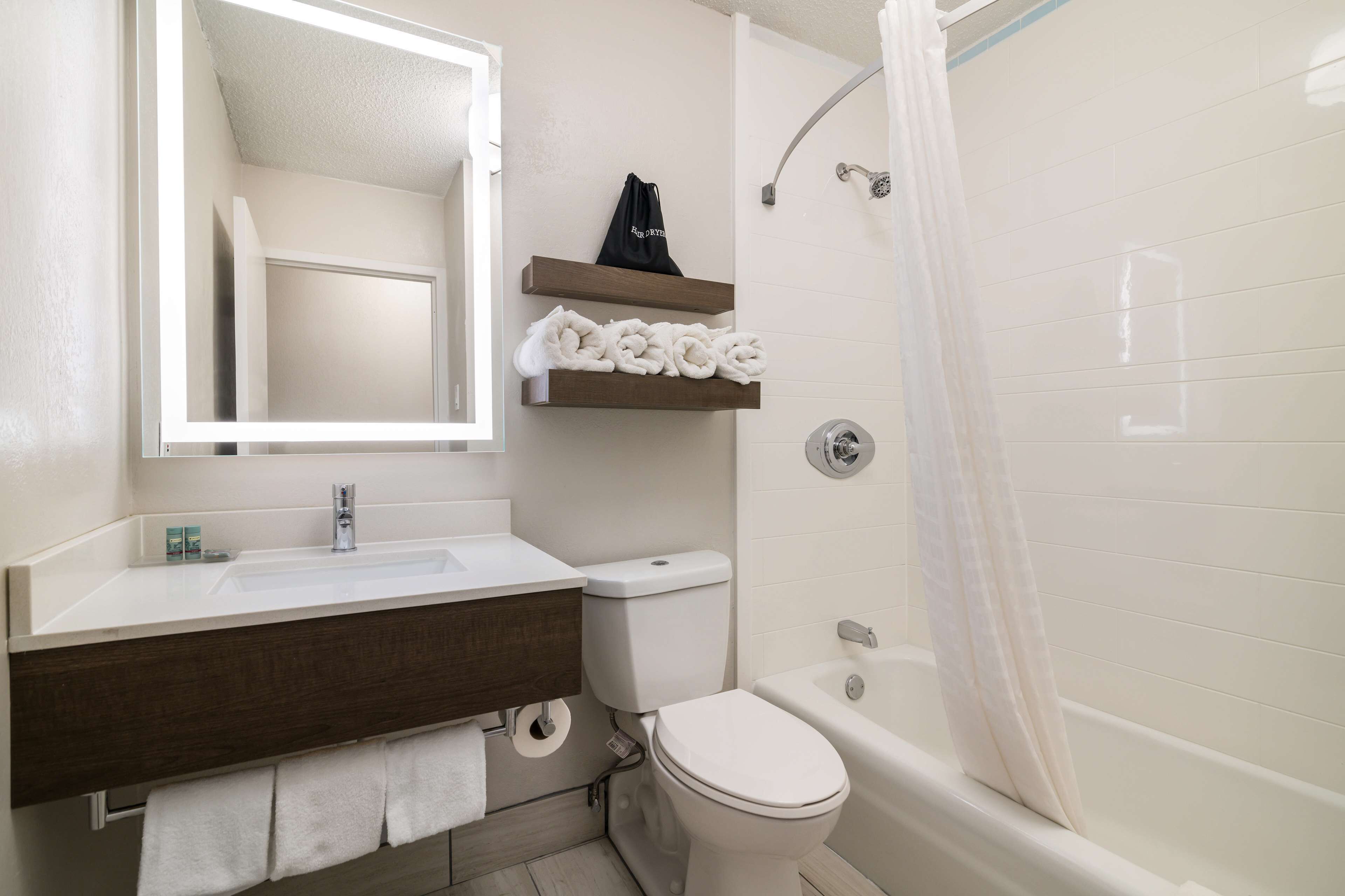 Un baño con lavamanos blanco, tocador de madera oscura, inodoro y bañera con cortina de ducha.