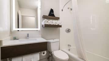 Un baño con lavamanos blanco, tocador de madera oscura, inodoro y bañera con cortina de ducha.