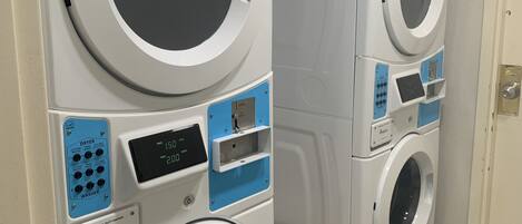 A row of commercial washing machines in a laundry room with a wooden bench.