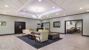 Un hall d’entrée spacieux agrémenté d’un lustre moderne, un coin salon avec des canapés et des fauteuils, une table basse en bois et un tapis foncé.