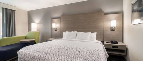 A hotel room with a large bed, a green armchair, a small table, and two bedside lamps.