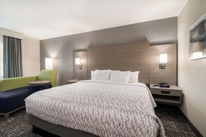 A hotel room with a large bed, a green armchair, a small table, and two bedside lamps. - Best Western Plymouth Inn-White Mountains (Campton)