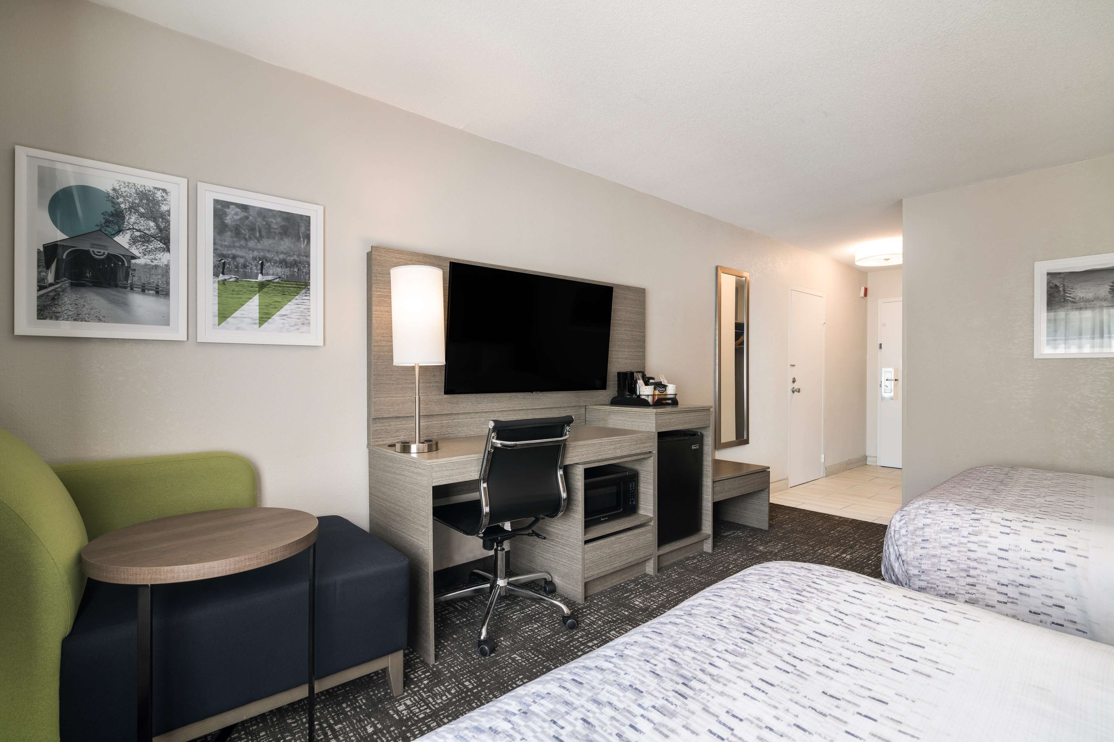Une chambre d’hôtel comprenant un lit, un bureau avec une chaise, une télévision et deux tableaux encadrés accrochés au mur.