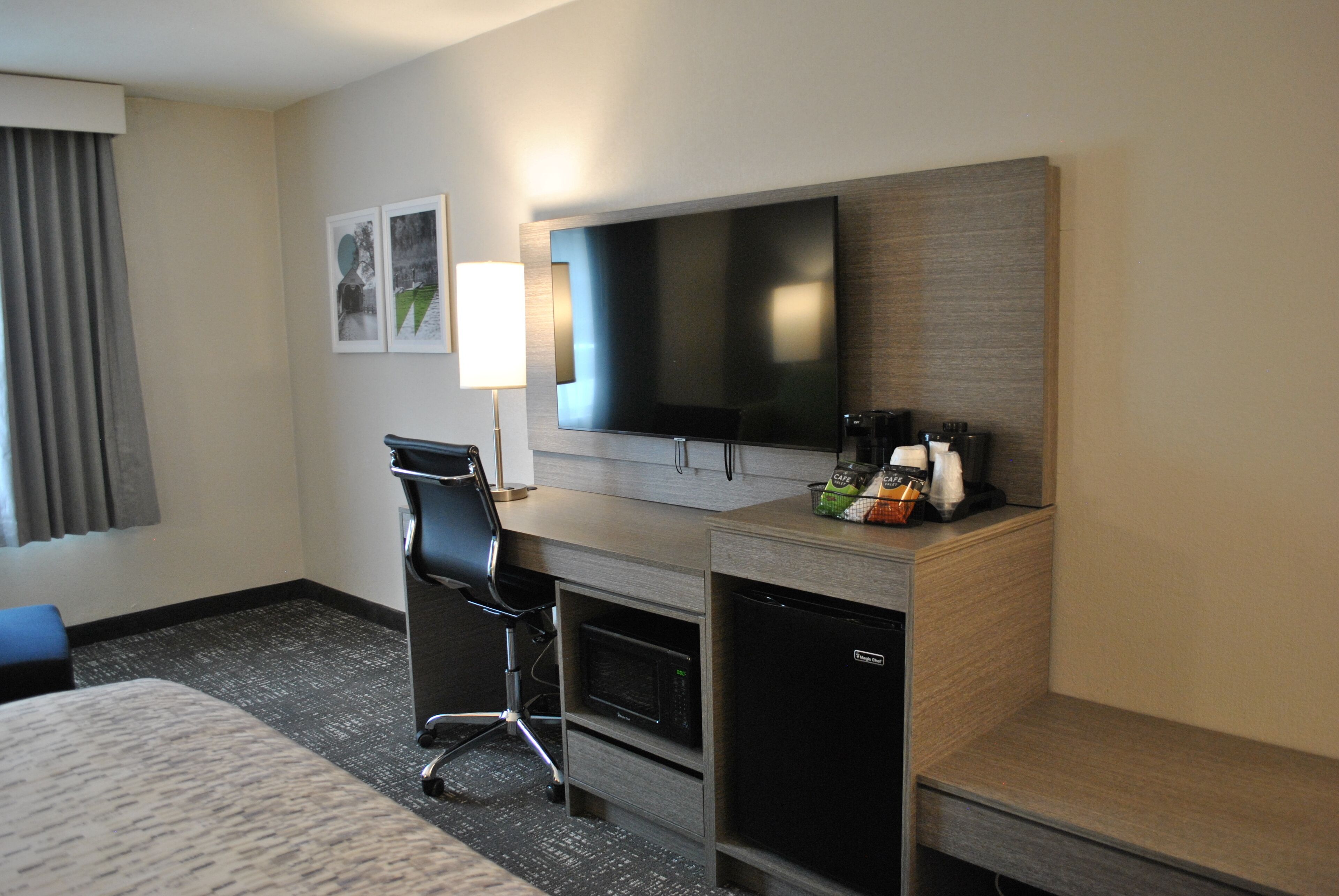 Habitación de hotel con cama, escritorio con silla, televisor de pantalla plana, microondas y cafetera.
