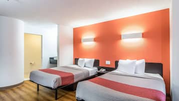 A hotel room with two beds, a wooden floor, and a bright orange accent wall.