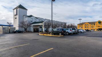 A parking lot with several cars, a building with a tower, and a yellow building in the background.