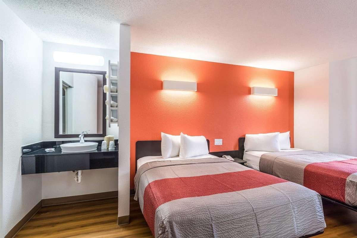 A hotel room with two beds, a bathroom with a sink, and a mirror.