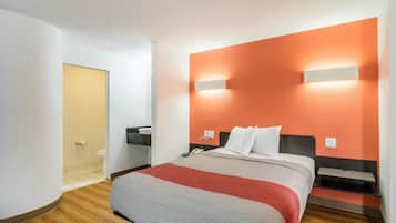 Ett hotellrum med en säng, sängbord, ett litet bord, en väggmonterad lampa och en dörr som leder till badrummet.
