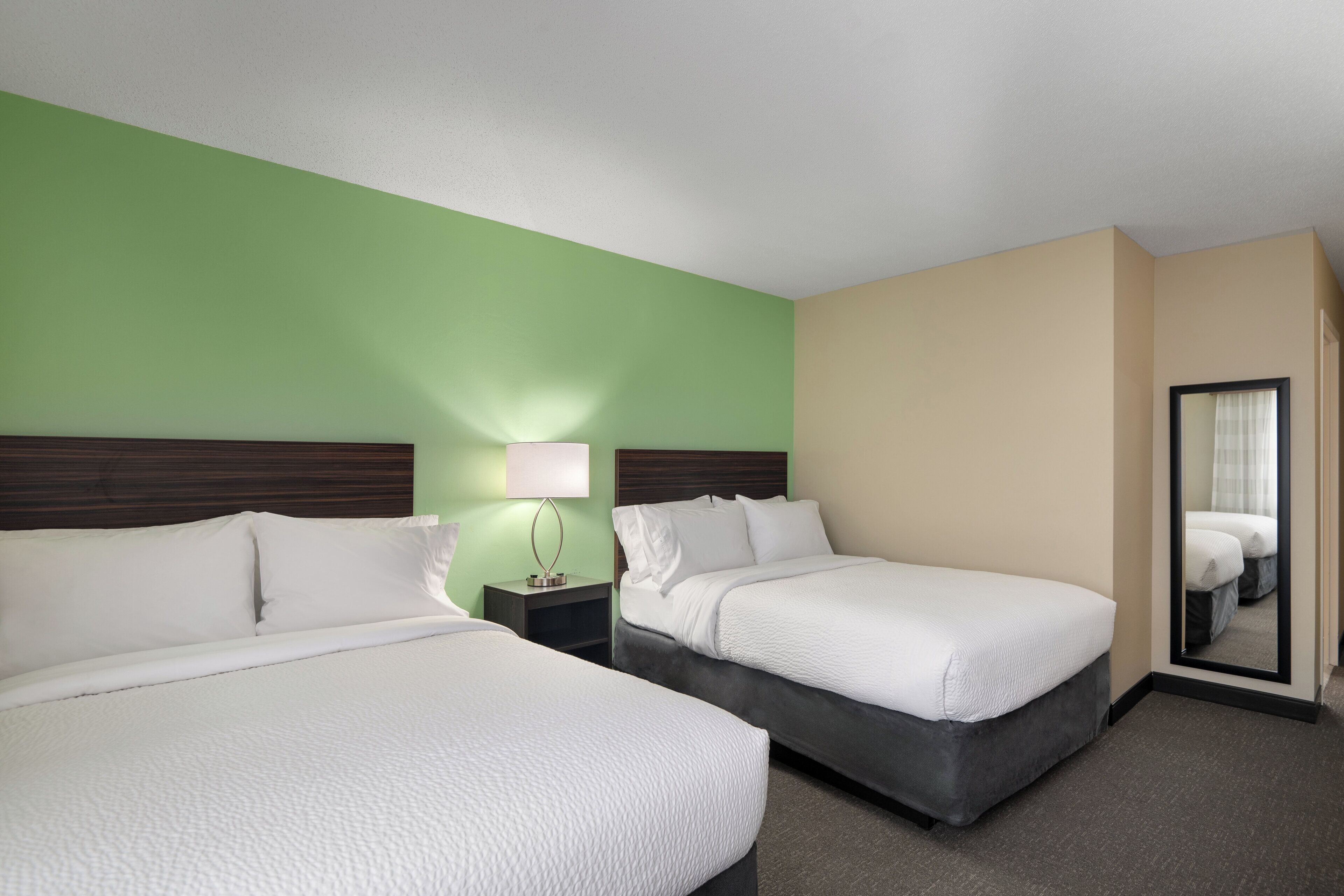 Habitación de hotel con dos camas, una mesita de noche con lámpara y un espejo.