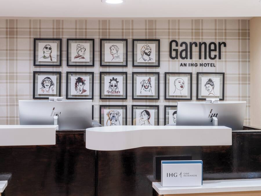 A hotel reception desk with framed portraits on the wall, a sign for IHG One Rewards, and a check-in counter.