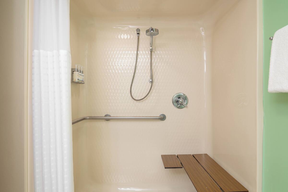 A shower area with a handheld showerhead, a grab bar, and a bench.