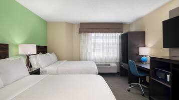 Habitación de hotel con dos camas, un escritorio, una silla, un televisor y una ventana con cortinas translúcidas.